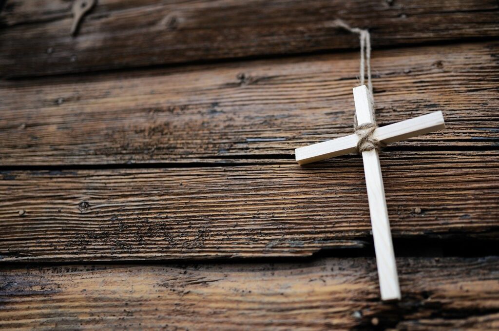 A small wooden cross, held together with twine, hanging on a wooden wall or fence. Christianity, faith, forgiveness
Image by congerdesign from Pixabay 