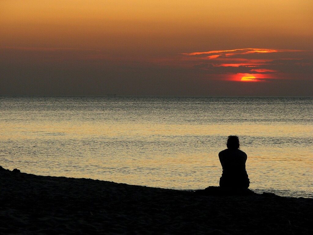 A woman silhouette sitting, looking out over an ocean, watching the sunset (or sunrise). Expectations. 
Image by czu_czu_PL from Pixabay