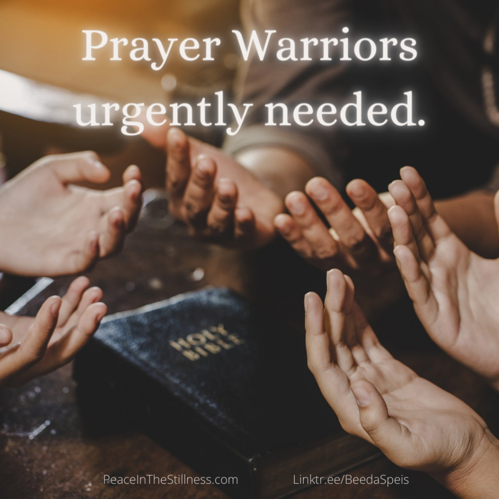 A group of people in a circle around a bible with their hands turned palms up to the heavens, in prayer. The words, "Prayer Warriors urgently needed" are at the top of the photo. By Beeda Speis for Peace In The Stillness blog.